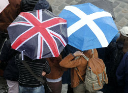 People shelter under a Saltire and a Union Jack umbrellas as they watch Officer Cadets from City of Edinburgh Universities Training Corps fire a 21-Gun Royal Salute at Edinburgh Castle to mark the 93rd Birthday of the Duke of Edinburgh.
