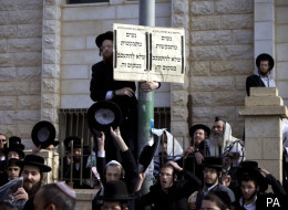 Ultra-Orthodox Jewish men gather around a sign that reads in Hebrew: