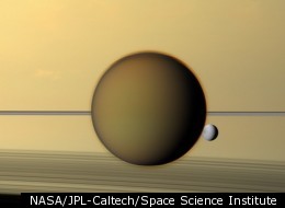 Saturn's fourth-largest moon, Dione, can be seen through the haze of the planet's largest moon, Titan, in this view of the two posing before the planet and its rings from NASA's Cassini spacecraft.