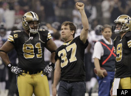 Former New Orleans Saints football player Steve Gleason raises his hand to the crowd before the first half of an NFL football game against the Houston Texans, Sunday, Sept. 25, 2011, in New Orleans. Saints quarterback Drew Brees (9) and defensive end Will Smith (91) look on. (AP Photo/Gerald Herbert)