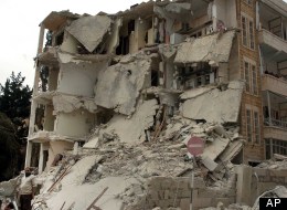 In this photo released by the Syrian official news agency SANA, a Syrian man, left, stands in front of a building that was damaged after two bombs exploded near a military compound, in the city of Idlib, northwestern Syria, Monday, April 30, 2012. (AP Photo/SANA)